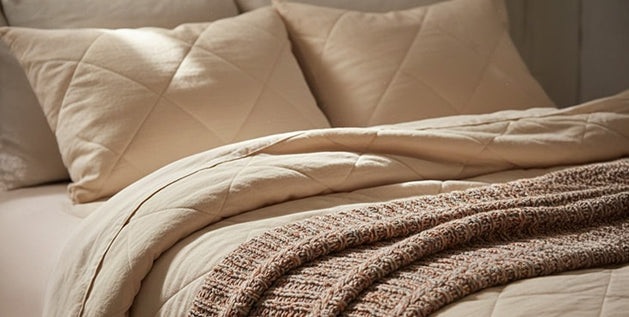 Cozy bedding ideas with layered quilted comforter, linen pillow shams, and a chunky knit throw blanket in neutral tones.