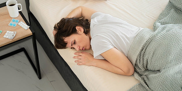 Woman lying awake and uncomfortable in bed, with sleep aid pills and coffee on the nightstand.