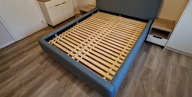 Slatted wooden foundation in an empty gray upholstered bed frame, a good base for a latex mattress.