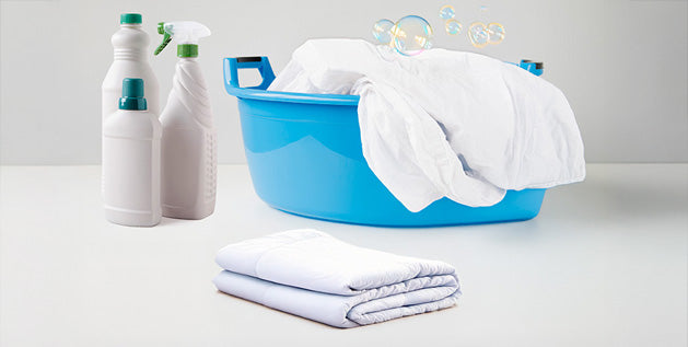 Washing sheets in a blue basin with detergent and spray bottles nearby, a folded clean sheet in front.