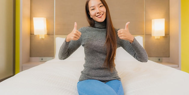 Woman sitting on a mattress giving two thumbs up after testing it for comfort and support at home.