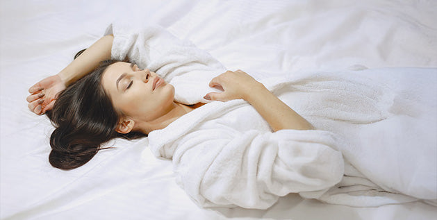 Woman lying on white bedding with arms raised above her head, sleeping without a pillow.
