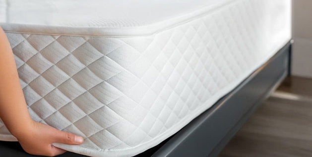 Hand lifting a mattress corner to inspect layers that affect its mattress weight limit and support quality.