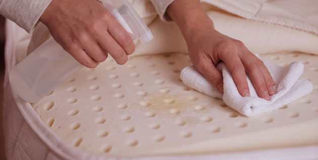 Person spot-cleaning latex mattress by gently blotting a spill with a cloth, showing how to care for your latex mattress.