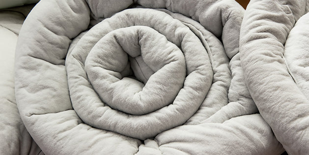 Light gray weighted blanket rolled into a spiral, showing its thick, soft, quilted texture.