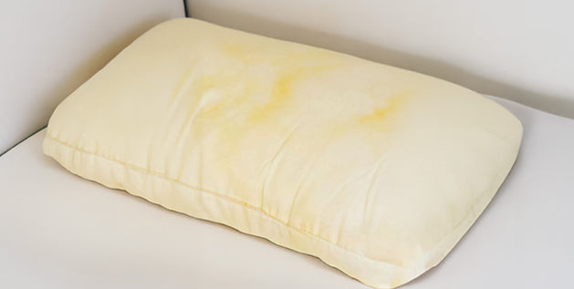 Yellow pillow stained with sweat and body oil discoloration resting on a white sofa cushion.