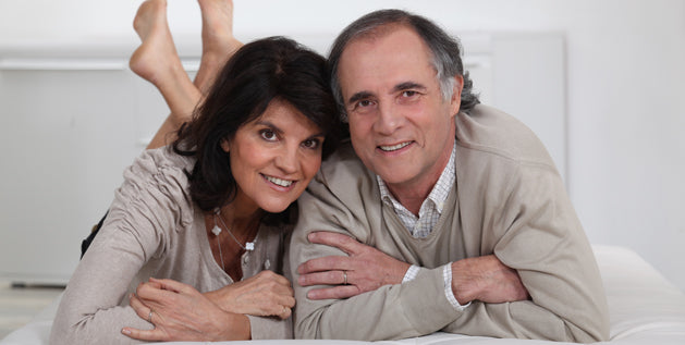Smiling man and woman lying close together on a white cushioned surface, with her bare feet raised behind her.