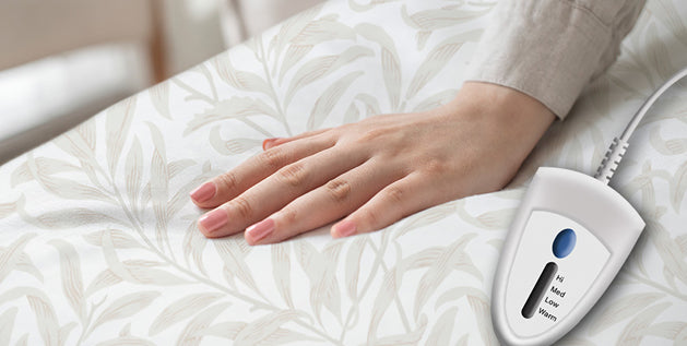 Hand resting on a patterned heated mattress pad with a bedside controller showing Hi, Med, Low, and Warm settings.