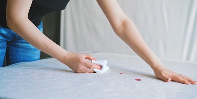 Woman blotting a fresh blood stain out of a mattress with a white cloth.