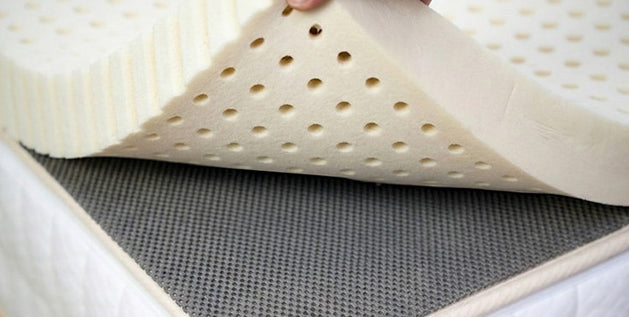 Hand lifting a latex mattress topper to show the grip pad used to keep the topper from sliding off the mattress.