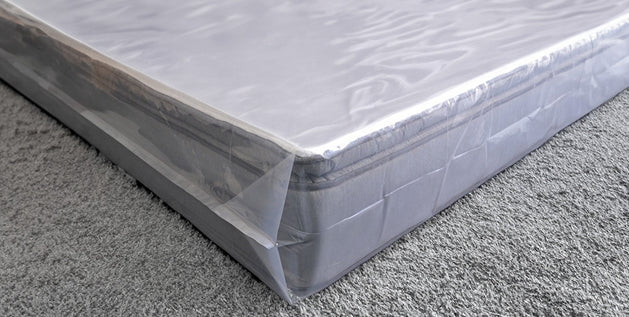 Mattress wrapped in clear plastic cover on a carpeted floor, ready for storage, showing how to store a mattress.